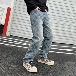 Op de afbeelding: Blauwe spijkerbroek met een ruitpatroon. De jeans wordt gecombineerd met sneakers met luipaardprint, zwarte veters en een crèmekleurige zool. De persoon draagt een zwart shirt met lange mouwen.