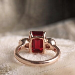 Pu&ograve; includere: Un anello in oro rosa con una pietra preziosa rosso intenso dal taglio rettangolare a smeraldo come pietra centrale. Il gambo dell'anello &egrave; liscio e lucido, con due piccole pietre rotonde incastonate ai lati della pietra centrale.
