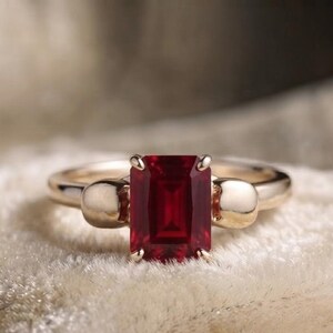 Pu&ograve; includere: Un anello in oro con una pietra preziosa rosso intenso taglio smeraldo tenuta da quattro griffe. La fascia &egrave; decorata su ciascun lato da un motivo a teschio in oro liscio e lucido che si collega direttamente alla montatura della pietra.