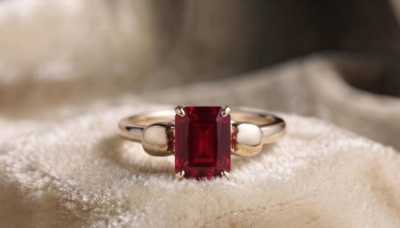 Pu&ograve; includere: Un anello in oro con una pietra preziosa rosso intenso taglio smeraldo tenuta da quattro griffe. La fascia &egrave; decorata su ciascun lato da un motivo a teschio in oro liscio e lucido che si collega direttamente alla montatura della pietra.