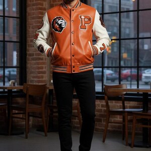 May include: A brown and white leather varsity jacket with a lion patch and the letter "P". The jacket has black and white striped trim and is worn with black pants and black boots. The jacket is a classic style.