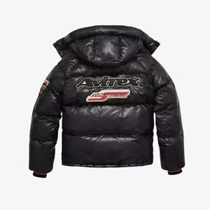 May include: Black puffer jacket with a hood. The jacket features the "Avirex" logo on the back in white and red. The jacket has a glossy finish and a red and black striped cuff.