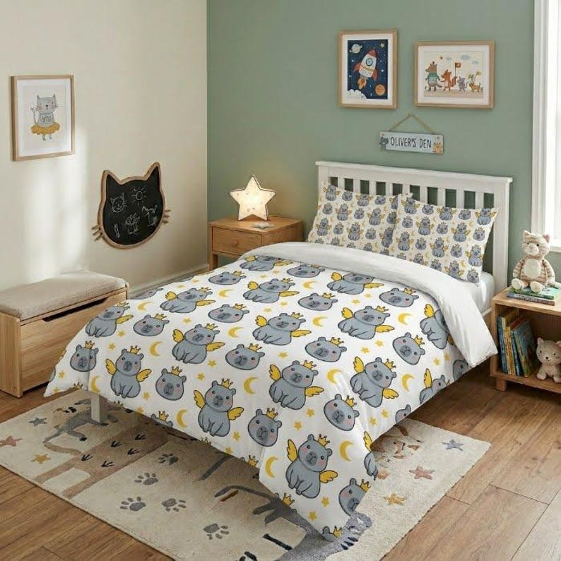 A colorful kids' bedroom showing a whimsical angel capybara-themed duvet cover and matching pillowcases, styled with a star-shaped lamp, rocket poster, and wooden floor.