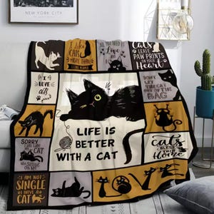 May include: A patchwork throw blanket with a cat theme. The design includes black cat illustrations and phrases like "Life is better with a cat". The color palette is cream, black, and gold. The blanket is designed to be used on a sofa or bed.