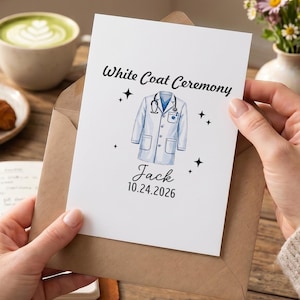 以下が含まれることがあります： 茶色の封筒に入った白いグリーティングカード。White Coat Ceremonyの文字、聴診器をかけた白衣のイラスト、Jackという名前、2026年10月24日の日付が印刷されており、小さな黒い四芒星のアイコンがアクセントとして添えられています。