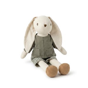Puede incluir: Un muñeco de peluche de conejo con orejas largas y caídas y un cuerpo blanco roto. Lleva una chaqueta verde y pantalones cortos a cuadros. Los pies del conejo son de color marrón y tiene ojos bordados y una pequeña nariz.