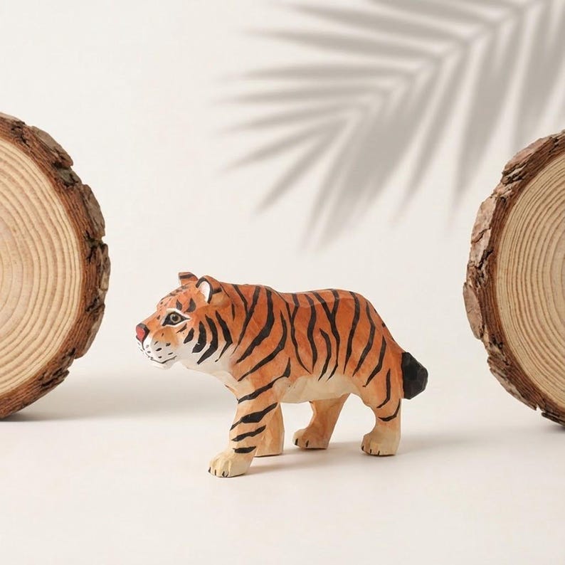K&ouml;nnte beinhalten: Handgeschnitzte Holz-Tigerfigur mit orangefarbenen und schwarzen Streifen, roter Nase und wei&szlig;en Akzenten. Der Tiger befindet sich in einer Laufhaltung. Zwei Holzscheiben rahmen den Tiger auf einer wei&szlig;en Oberfl&auml;che ein.