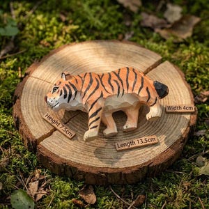 K&ouml;nnte beinhalten: Handgeschnitzte Holz-Tigerfigur mit orangefarbenen und schwarzen Streifen, stehend auf einer Holzscheibe. Der Tiger ist 13,5 cm lang, 7,5 cm hoch und 4 cm breit. Der Hintergrund ist gr&uuml;nes Moos.