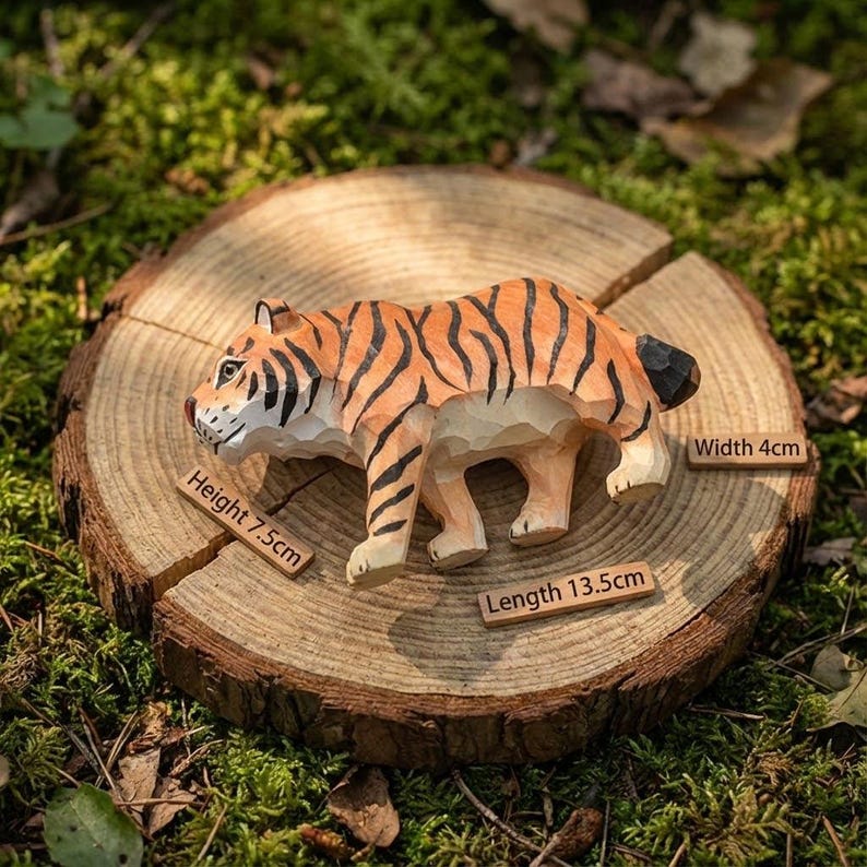 K&ouml;nnte beinhalten: Handgeschnitzte Holz-Tigerfigur mit orangefarbenen und schwarzen Streifen, stehend auf einer Holzscheibe. Der Tiger ist 13,5 cm lang, 7,5 cm hoch und 4 cm breit. Der Hintergrund ist gr&uuml;nes Moos.