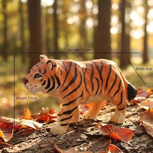 Puede incluir: Figura de tigre de madera tallada a mano, de 13,5 cm de largo, 4 cm de ancho y 7,5 cm de alto. El tigre tiene rayas naranjas y negras, una nariz roja y está posado sobre una superficie de madera con hojas. Es un objeto decorativo.