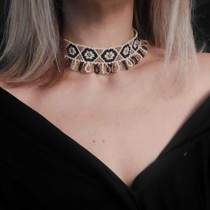 May include: A beaded choker necklace with a geometric pattern. The necklace features a repeating design of black, gold, and white beads. The choker is worn around the neck and is set against a black background.