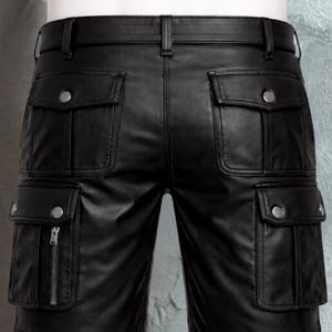 Pu&ograve; includere: Pantaloni cargo in pelle nera con multiple tasche e dettagli con bottoni argentati. I pantaloni hanno una cintura con passanti e una chiusura con cerniera su una delle tasche. La pelle appare liscia e il design &egrave; su misura.