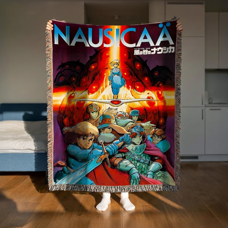 a person holding up a colorful, cartoon-style blanket with the title "Nausicaä" prominently displayed.