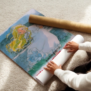 A person is sitting on the floor and placing a rolled-up poster under a drawing of a woman with long blonde hair.