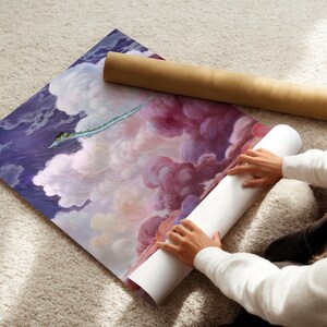 A person is unfolding a large piece of paper with a painting of a colorful, cloud-filled sky on it, which appears to be a large poster or canvas.