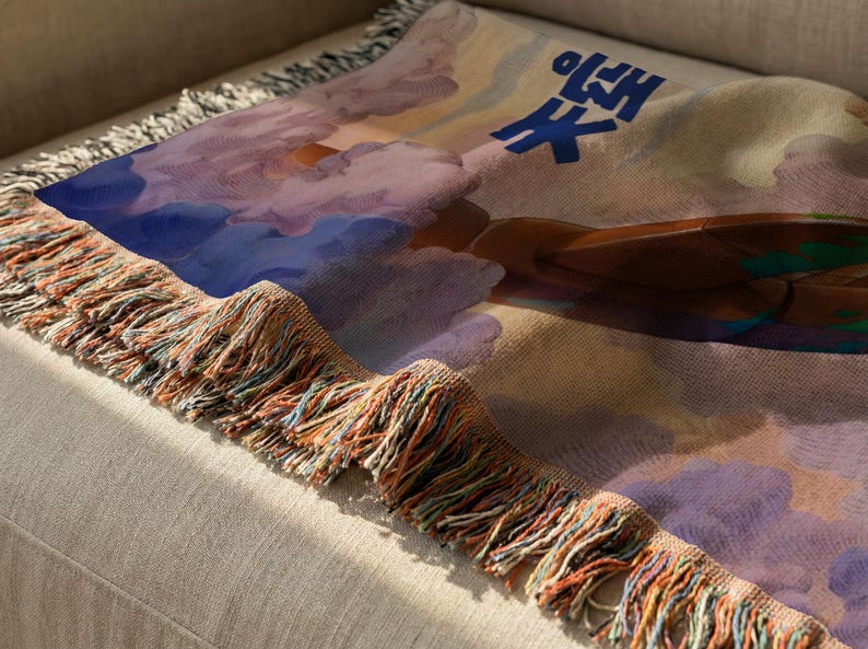 a colorful, abstract design with a mix of blue, purple, and orange colors, along with a cloud-like shape. The design appears to be a textile or fabric item, possibly a blanket or throw, with a fringed edge.