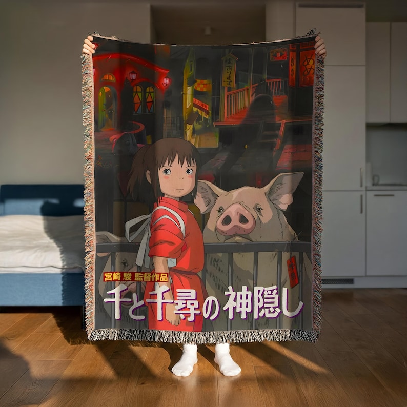 A person is holding a large blanket featuring an illustration of a young girl and a pig, with Japanese text on the blanket.