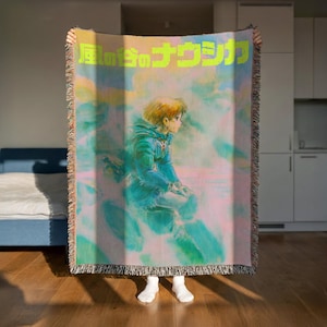 A person is holding up a colorful blanket with a cartoon character on it, which appears to be a piece of artwork or a decorative item.