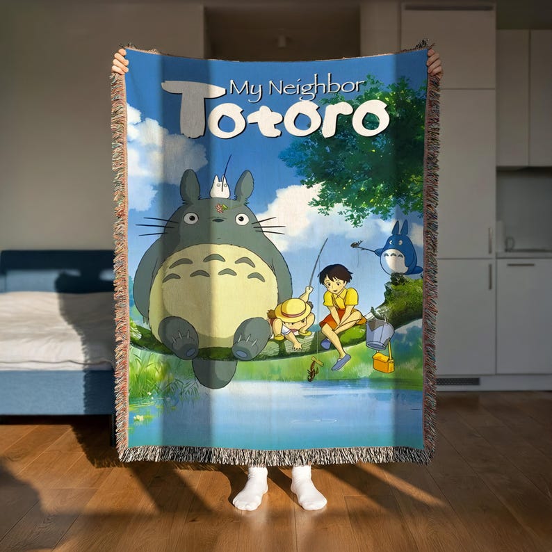 A person is holding up a colorful blanket featuring the character Toto from the animated film "My Neighbor Totoro".