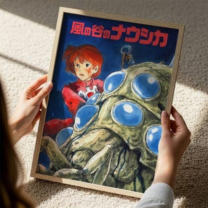 A person is holding a framed artwork depicting a character with red hair and a red outfit, standing in front of a large, colorful creature with blue eyes.