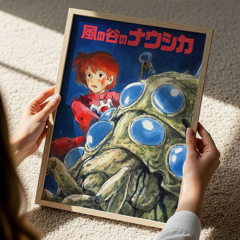 A person is holding a framed artwork depicting a character with red hair and a red outfit, standing in front of a large, colorful creature with blue eyes.