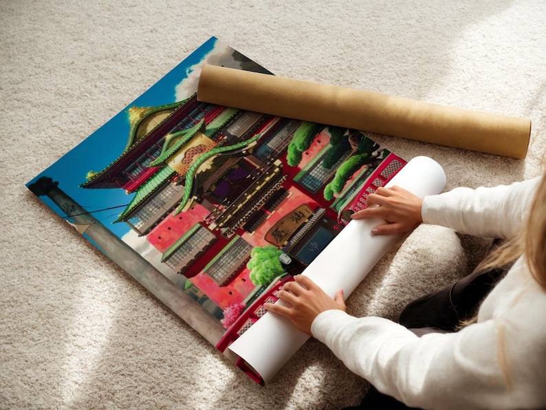 A person is sitting on the floor and rolling up a large poster of a colorful Asian building.