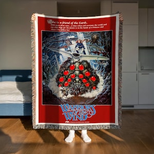 A person is holding up a large poster or artwork featuring a fantastical scene with a large creature, red objects, and a spaceship. The poster has a red background with white text and graphics.