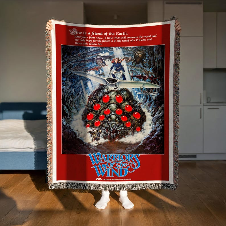 A person is holding up a large poster or artwork featuring a fantastical scene with a large creature, red objects, and a spaceship. The poster has a red background with white text and graphics.