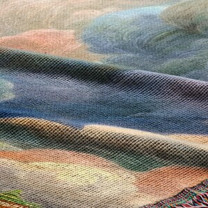 The image is a close-up of a textured fabric with a colorful, abstract pattern. The fabric appears to be a woven material, possibly a blanket or a textile. The pattern on the fabric is a mix of various colors and shapes, creating a visually interesting and dynamic design.