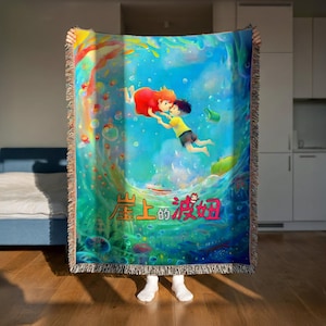 A person is holding up a colorful, vibrant blanket with an illustration of two characters floating in a blue ocean scene.