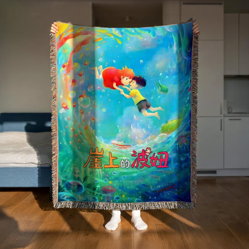 A person is holding up a colorful, vibrant blanket with an illustration of two characters floating in a blue ocean scene.