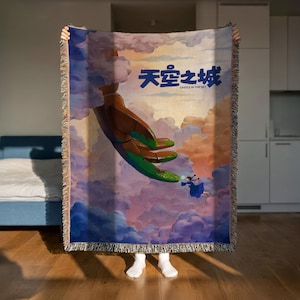 A person is holding up a colorful tapestry or blanket with a painting of a hand reaching out towards a person in the sky.