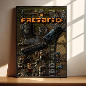 Puede incluir: Póster enmarcado con la palabra "Factorio" en letras naranja. La obra de arte representa una escena industrial detallada con un tren azul sobre vías, maquinaria y tuberías. El póster se exhibe sobre una superficie de madera.