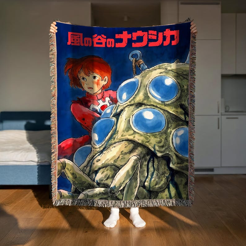 A person is holding up a large blanket with an illustration of a character from a Japanese animated film.