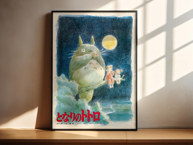 The image is a framed poster featuring a whimsical illustration of a large, green creature with horns and a yellow moon in the background, accompanied by two smaller figures.