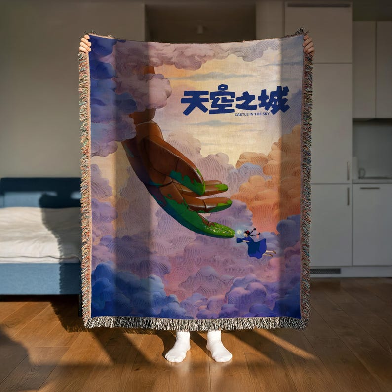 A person is holding up a colorful tapestry or blanket with a painting of a hand reaching out towards a person in the sky.