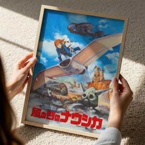 A person is holding a framed poster featuring an illustration of a character riding a winged vehicle through a fantastical landscape with various other fantastical elements.