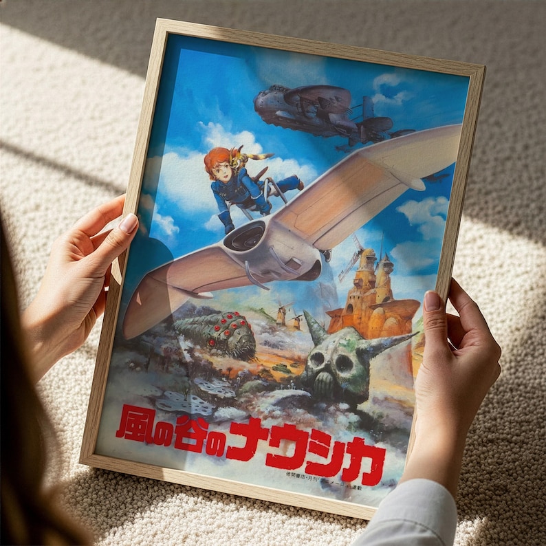 A person is holding a framed poster featuring an illustration of a character riding a winged vehicle through a fantastical landscape with various other fantastical elements.