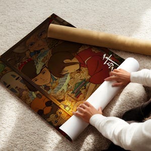 A person is holding a roll of paper and unfolding a poster featuring colorful artwork.