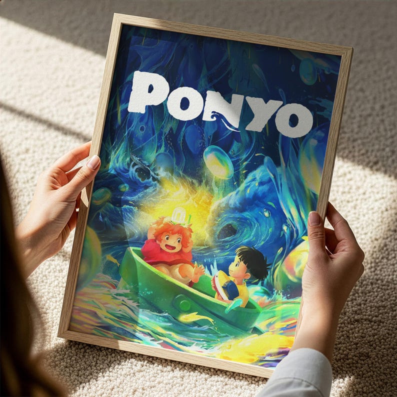 A person is holding a framed poster of the animated film "Ponyo". The poster features colorful artwork depicting a character in a boat surrounded by a fantastical underwater scene.