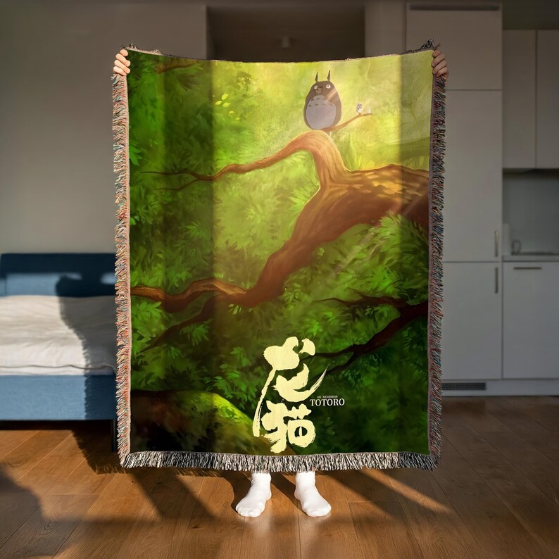 A person is holding up a large, colorful blanket with a painting of a tree and an owl on it.