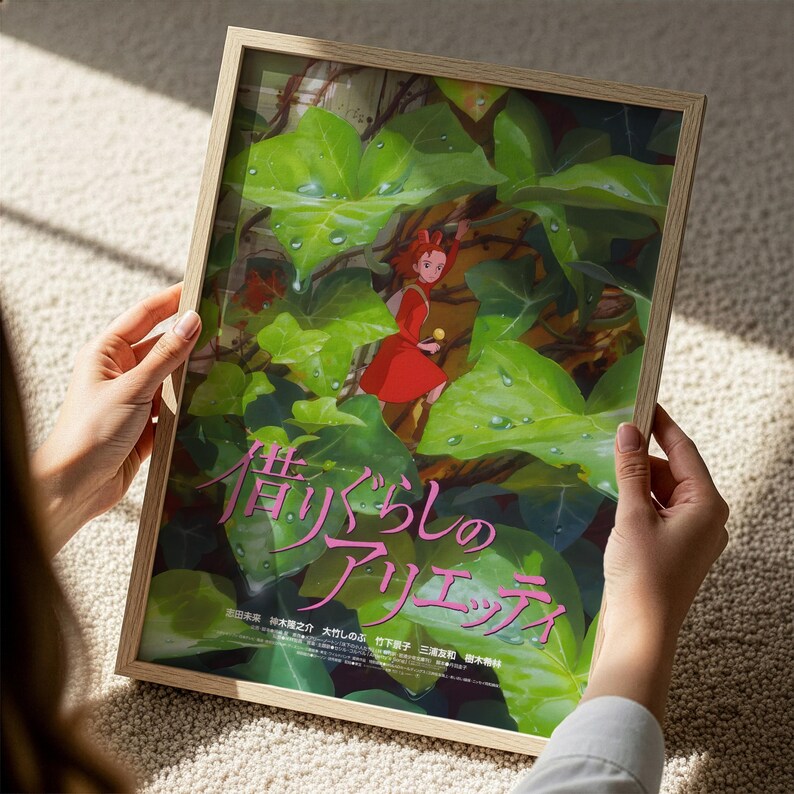 A person is holding a framed poster with an illustration of a character in a red dress standing amidst green leaves.