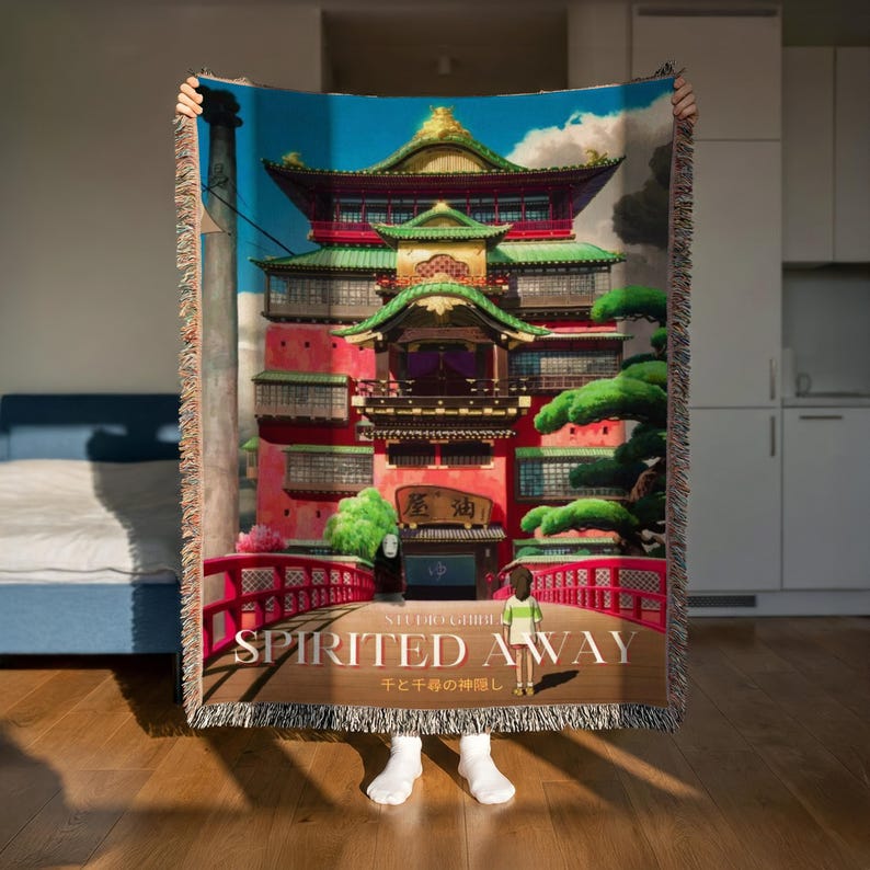 A person is holding up a colorful tapestry or blanket that features a large image of a traditional Japanese temple or pagoda.