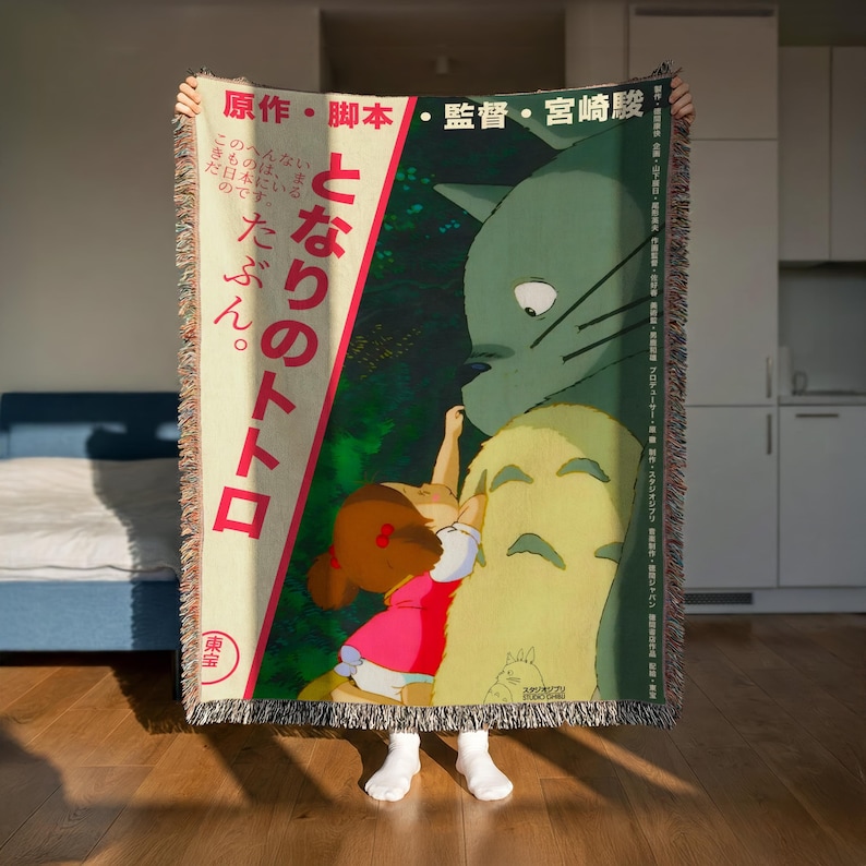 A person is holding up a colorful blanket featuring an illustration of a young girl and a cat.
