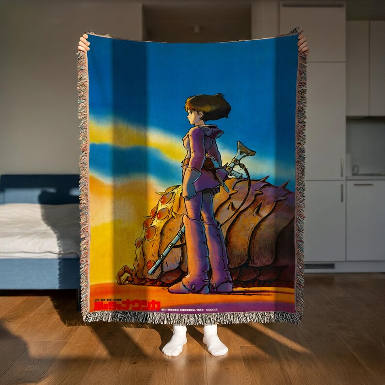 A person is holding up a colorful blanket with an illustration of a woman standing in front of a desert landscape.
