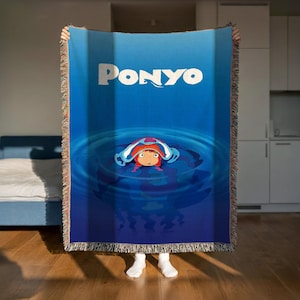 A person is holding up a large blue blanket with the word "Ponyo" printed on it, which features an illustration of a character in a blue pool.