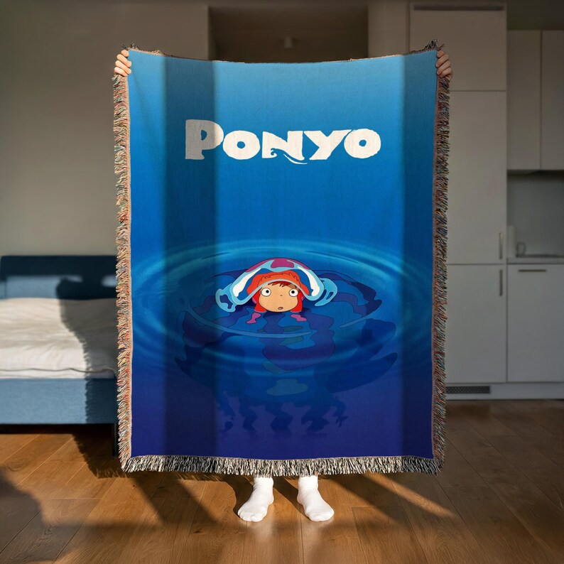 A person is holding up a large blue blanket with the word "Ponyo" printed on it, which features an illustration of a character in a blue pool.