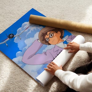 A person is holding a rolled-up poster featuring an illustration of a young boy with glasses and a hat, looking up at an airplane in the sky.