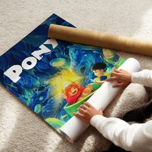 A person is holding a roll of paper and a poster featuring colorful cartoon characters, including Pony, on a carpeted floor.