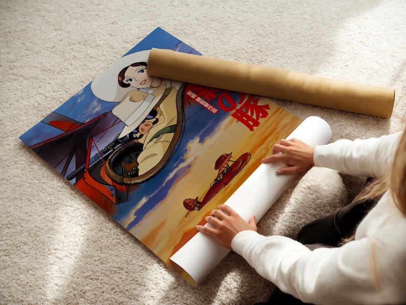 A person is sitting on the floor and placing a roll of paper under a poster featuring an illustration of a character and a scene with a red airplane.